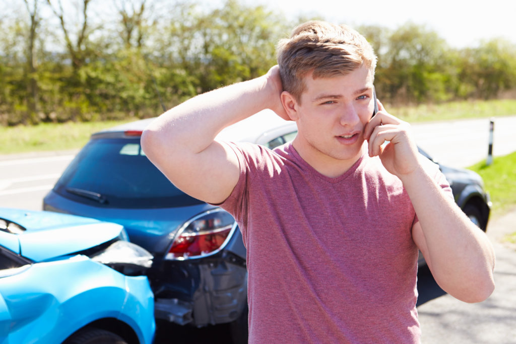 Young man standing next to car crash